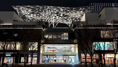 Night-view-of-a-modern-shopping-center-with-intricate-canopy-lighting,-trees-in-foreground-in-Yokohama,-Japan