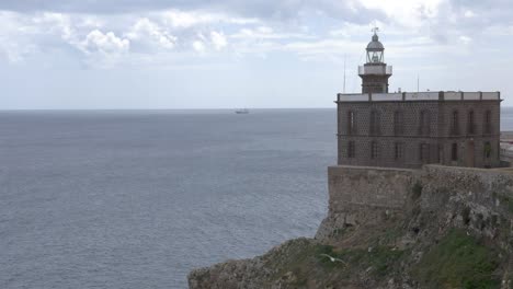 Leuchtturm-Von-Melilla-Mit-Dem-Mittelmeer-Im-Hintergrund-Und-Einem-Frachtschiff