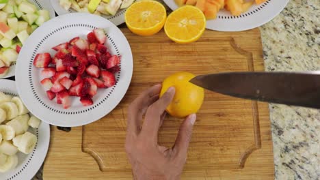 Top-view-of-male-hands-cutting-oranges-into-equal-halves-on-cutting-board