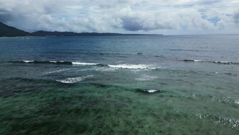 Coastal-view-of-Agoho-San-Andres-with-clear-waters-and-surfers,-Catanduanes,-Philippines,-cloudy-skies