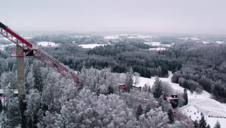 Aerial-shot-over-forest-with-Tehvandi-ski-jump-tower-visible-in-very-cold-winter-weather-and-snowy-trees-everywhere