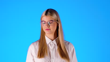 Blonde,-Smart-Aussehende,-Kaukasische-Junge-Frau-Spielt-Mit-Einem-Orangefarbenen-Porträt-Im-Lehrerstil,-Aufgenommen-Mit-Brille-Im-Blauen,-Unendlichen-Chroma-Hintergrundstudio