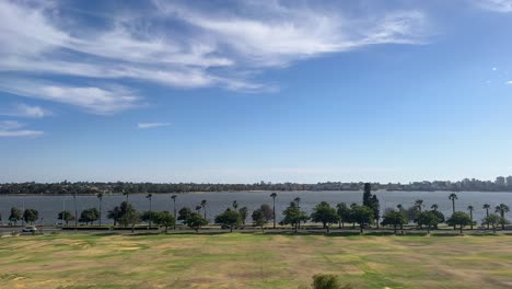 Riverside-Drive-in-Perth,-Western-Australia-with-palm-trees-along-the-Swan-River-with-wispy-clouds-above-on-a-blue-sky-day