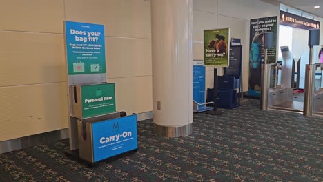 Frontier-Airlines-bag-sizer-and-other-signs-with-passengers-walking-by-in-the-background-in-airside-1-at-MCO,-Orlando-International-Airport