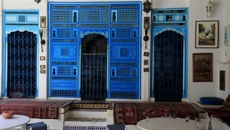 Traditional-Tunisian-courtyard-in-Sidi-Bou-Said-with-blue-doors,-white-walls,-and-decorative-rugs,-sunny-day