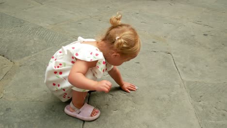 A-little-blonde-toddler-with-pigtails-is-wiping-the-stone-street-with-a-tissue