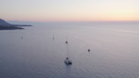 Vista-Aérea-De-Barcos-En-Mar-Tranquilo-Con-Gente-Durante-La-Puesta-De-Sol,-Cefalu,-Sicilia,-Italia