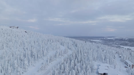 Drone-tilting-toward-cars,-driving-in-middle-of-snowy-mountain-forest-of-Lapland