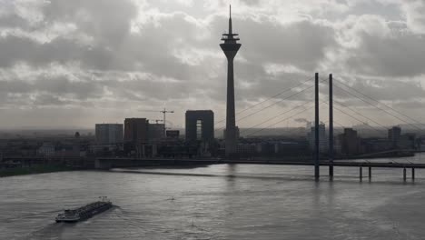 Barcaza-De-Envío-Navegando-Por-El-Río-Rhein-Con-La-Torre-Al-Fondo,-Dusseldorf,-Alemania