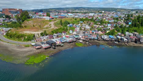 Aerial-orbit-establishing-of-the-stilt-houses-in-Castro,-Chiloé-on-a-sunny-and-clear-day,-low-tide-Chile