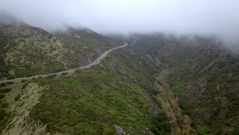 Santa-Monica-Mountains-in-Malibu,-California-with-traffic-driving-on-road-and-drone-video-moving-forward-and-down