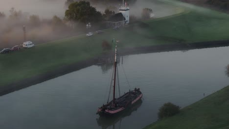 Aerial-view-of-traditional-wooden-sailing-boat-in-canal-during-a-misty-morning,-IJsselmeer,-Netherlands