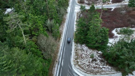 Aerial-view-of-car-driving-through-rural-snowy-streets