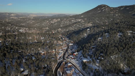 Downtown-old-historic-Evergreen-Colorado-Denver-aerial-drone-cinematic-fresh-snow-dusting-cold-white-scenic-landscape-dam-lake-traffic-driving-around-house-ice-skating-sunset-bluesky-backward-motion