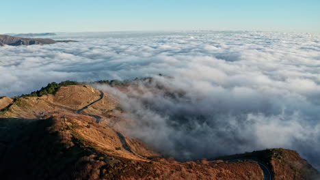 Un-Camino-Sinuoso-En-Una-Montaña-Sobre-Las-Nubes-Al-Amanecer,-Vista-Aérea