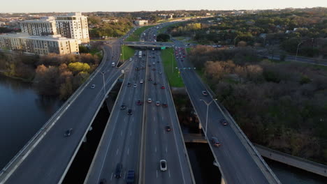 Aerial-view-following-cars-and-traffic-as-they-commute-and-cross-highway-bridge-over-a-river