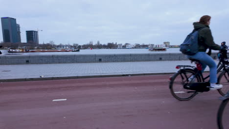 A-couple-rides-a-bicycle-together,-showcasing-the-casual-and-intimate-nature-of-Amsterdam's-primary-mode-of-transportation,-with-the-city's-waterfront-as-a-backdrop