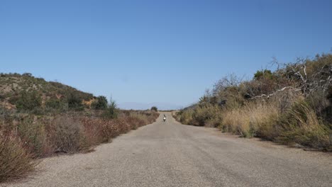 high-desert-road-with-motorcycle-passing,-coming-towards-with-camp-gear,-near-lake-elsinore-and-ortega-highway-in-Southern-California