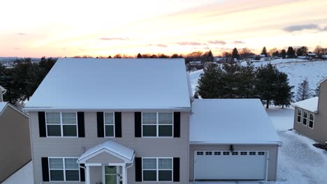 Bright-orange-sunset-over-a-snowy-suburban-home-with-a-two-car-garage