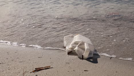 Discarded-plastic-bottle-on-sandy-beach-with-gentle-waves-in-the-background,-environmental-issue