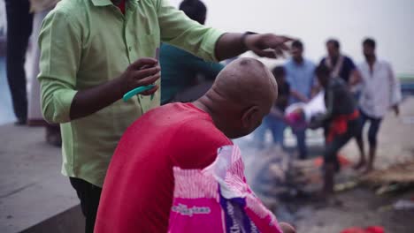 Vista-Lateral-De-Un-Peluquero-Local-Cortando-El-Cabello-En-Varanasi-Quemando-Ghat-Durante-La-Noche-En-La-India