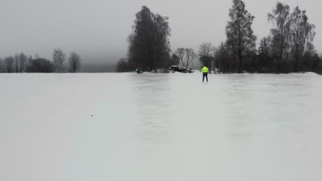 Flying-backward-above-frozen-field-with-shiny-ice-layer,-person-stand