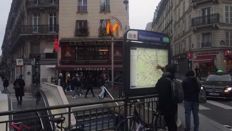 People-walk-by-Poissonière-metro-station-in-Paris,-woman-looks-at-map