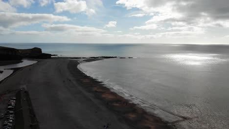 Aerial-decending-shot-over-Budleigh-Salterton-Beach-Devon-England-with-the-sun-shimmering-off-the-calm-sea