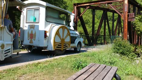 Small-tour-train-from-the-luna-park-Obilic-passing-over-the-old-iron-bridge,-crossing-the-Djetina-river-Uzice