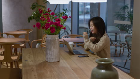 Una-Joven-China-Asiática-Habla-Alegremente-Y-Sonríe-Durante-Una-Llamada-En-Línea-En-Un-Café