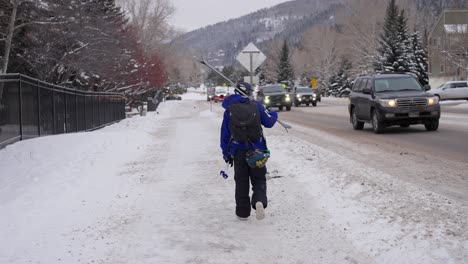 Rückansicht-Eines-Skifahrers,-Der-An-Einem-Kalten-Wintertag-An-Der-Straße-Und-Fahrenden-Fahrzeugen-Entlang-Läuft