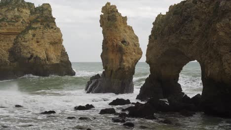 Large-waves-crashing-against-the-rocks-of-the-coast-eroding-and-forming-natural-arches-and-rock-bridges-at-Ponta-da-Piedade,-Algarve-in-Portugal