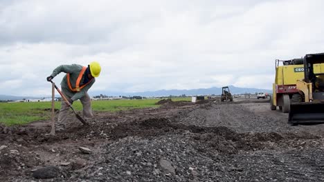 Trabajador-Paleando-Tierra-Cerca-De-Vehículos-De-Construcción-En-Un-Día-Nublado,-Argentina-Rural