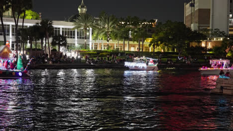 Flashing-holiday-light-bulbs-and-string-lights-reflect-off-water-as-onlookers-enjoying-parade