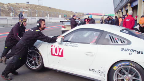 Pit-lane-crew-pulling-in-an-expensive-sports-car,-stock-car-competition,-Porsche