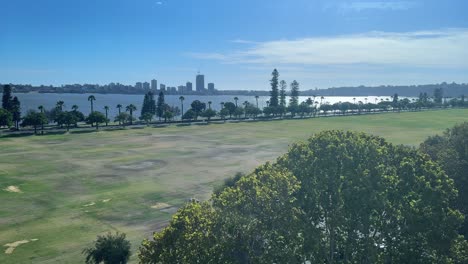 View-above-and-along-Langley-Park-in-Perth,-Western-Australia-to-the-Riverside-Drive-foreshore-from-an-office-building-with-blue-sky-and-vast-expanse-of-green-lawn-next-to-the-Swan-River