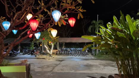 Colourful-lanterns-hanging-from-a-tree-outside-the-Odyssey-Hotel-in-Hoi-An,-Vietnam-looking-out-to-a-bike-rack