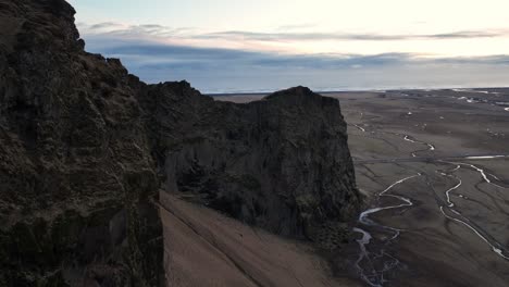 Aerial-view-over-a-scenic-cliff-on-a-mountain-in-Iceland,-with-a-dramatic-evening-cloudscape-and-birds-flying