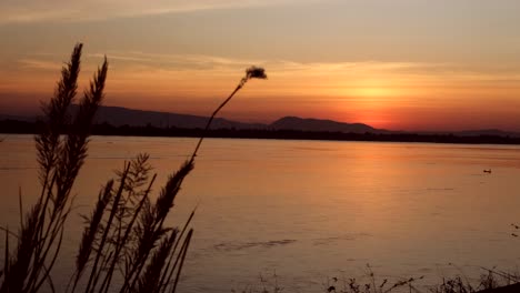 A-tranquil-landscape-captured-in-4K,-showcasing-a-vast-lake,-towering-mountain,-and-an-evolving-ambiance-as-the-sun-gracefully-descends,-casting-the-scene-into-a-dramatic-display-of-nature