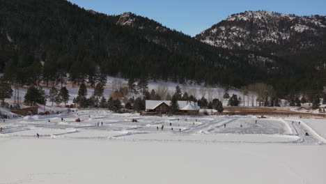 Ice-skating-skate-hockey-rink-lake-pond-hockey-winter-Etown-Evergreen-Lake-house-Denver-golf-course-Colorado-aerial-cinematic-drone-sunny-bluesky-morning-winter-fresh-snow-slowly-pan-up-reveal-forward