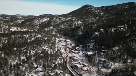 Downtown-old-historic-Evergreen-Colorado-aerial-drone-cinematic-winter-fresh-snow-cold-white-scenic-landscape-near-dam-lake-traffic-driving-around-house-ice-skating-late-morning-bluesky-forward-motion