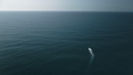 Aerial-shot-of-a-small-boat-all-alone-out-in-the-vast-ocean-under-sunlight