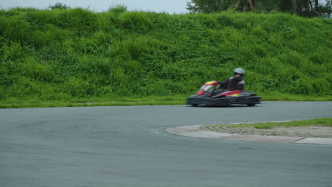 Guys-in-go-karts-flying-through-corner-of-race-circuit,-following-each-other