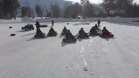 Start-of-go-kart-race-on-snow-and-ice-track-passing-under-drone,-Norway