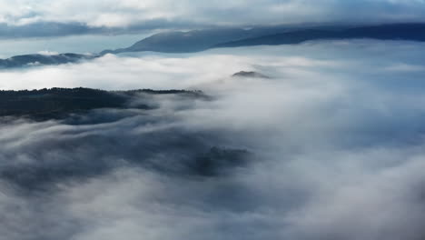 Misty-mountains-with-flowing-clouds-at-sunrise,-ethereal-nature-scene,-aerial-view