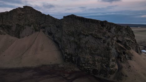 Aerial-view-over-a-scenic-cliff-on-a-mountain-in-Iceland,-with-a-dramatic-evening-cloudscape