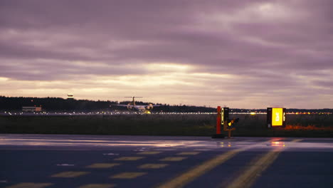 DeHavilland-Dash-8-Q400-landing-on-Tallinn-airport-runway-in-red-sunset-with-taxiway-signs-and-runway-warning-lights-in-foreground