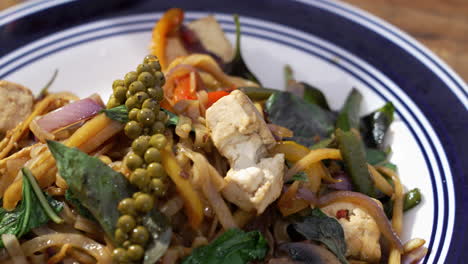 Tabletop-of-traditional-Pad-Kee-Mao-with-tofu-topped-with-fresh-thai-basil-and-green-peppercorns,-close-up-slider-4K