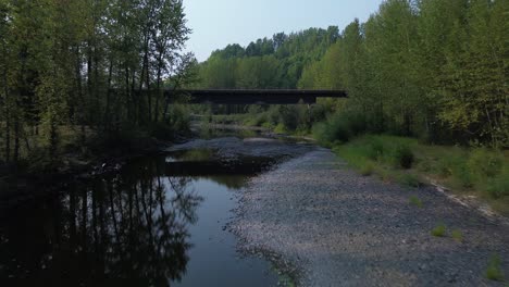 Niedrig-Fliegende-Drohne-Entlang-Des-Bulkley-River-Mit-Einer-Niedrigen-Brücke-überquert-Und-Alpinen-Bäumen-Auf-Beiden-Seiten-In-Einer-Natürlichen-Umgebung-In-Der-Nähe-Von-Houston,-Northwood-Picknickplatz,-Kanada