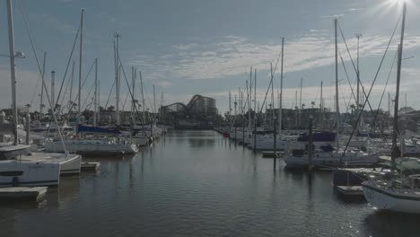 A-low-level-aerial-view-reveals-sailboats-in-their-slips-at-Kemah-Boardwalk-Marina,-set-against-a-backdrop-of-blue-skies-and-white-clouds-in-Kemah,-Texas